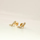 Gold high-heeled shoe earrings with rhinestone details on a beige background