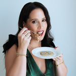 Woman in a green dress eating from a white plate with gold accents against a light gray background