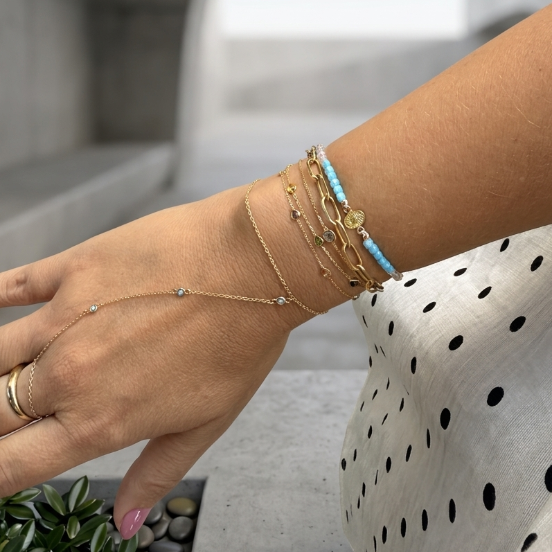 Lifestyle photo of a wrist wearing a 14K solid yellow gold Virgen Milagrosa multicolor 3 mm square shape quartz light purple macramé bracelet layered with delicate gold bracelets and a turquoise beaded bracelet.