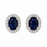 Pair of solid 14K white gold oval natural blue sapphire stud earrings surrounded by sparkling natural pavé diamond halos, front view.
