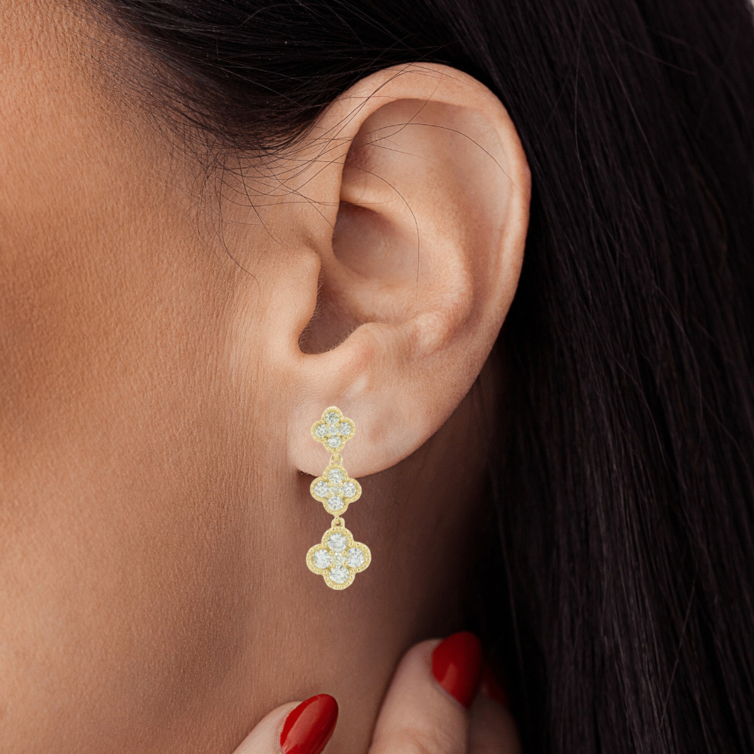 Close-up of an ear wearing a gold earring with red nail polish on the hand.