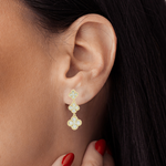 Close-up of an ear wearing a gold earring with red nail polish on the hand.