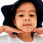 Little girl wearing layered sterling silver necklaces, including a blue evil eye choker and personalized initial necklaces, with sterling silver stud earrings and a navy bucket hat. Children’s fine jewelry styled for everyday wear.