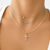 14K white gold diamond cross pendant necklace layered with a white gold evil eye necklace and a white gold bezel solitaire choker on model, minimalist fine jewelry stack.