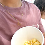 Person holding a bowl of popcorn wearing a gold necklace with a pendant.