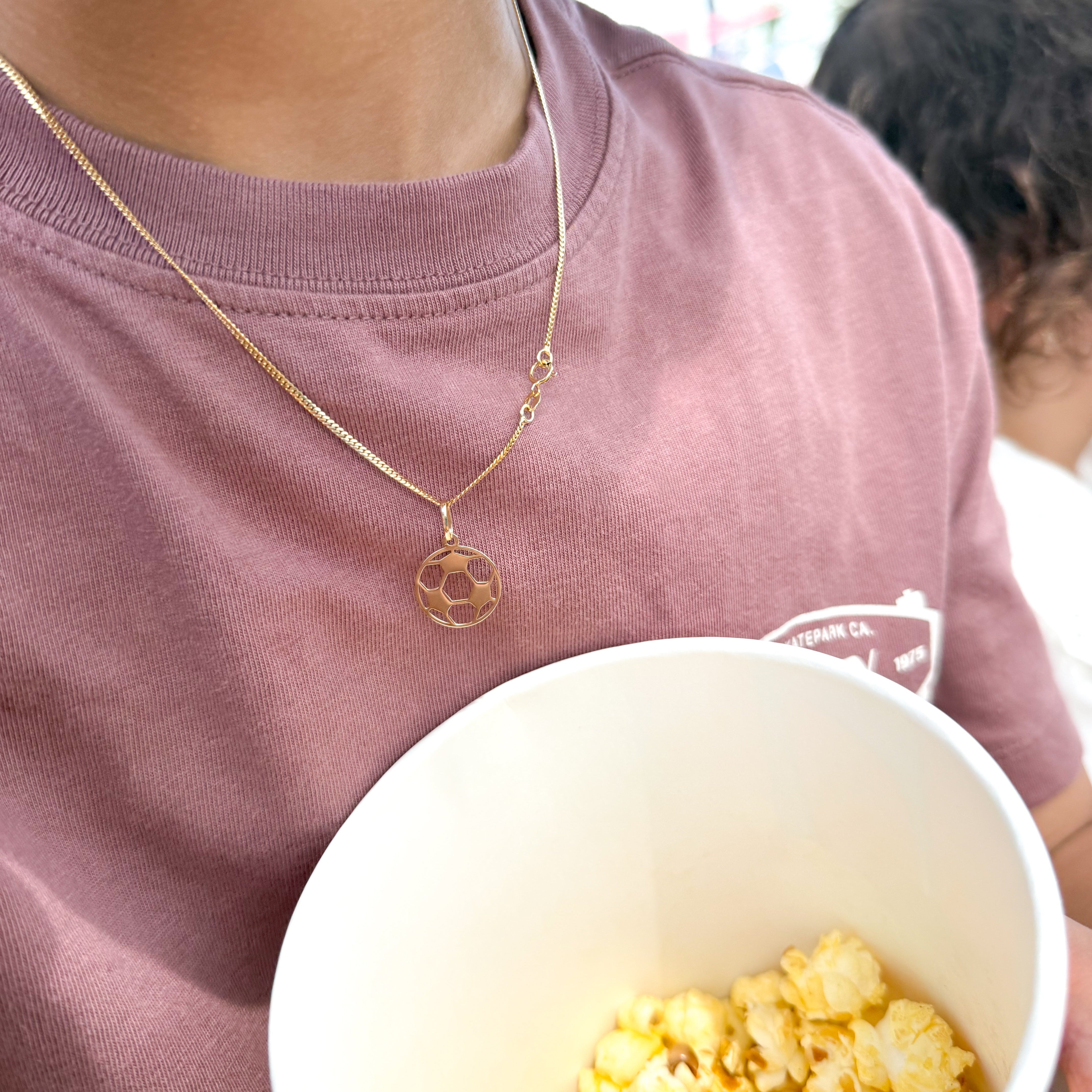 Person holding a bowl of popcorn wearing a gold necklace with a pendant.