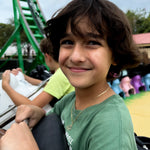 Child in a green shirt smiling in a roller coaster while wearing a chain with a soccer pendant