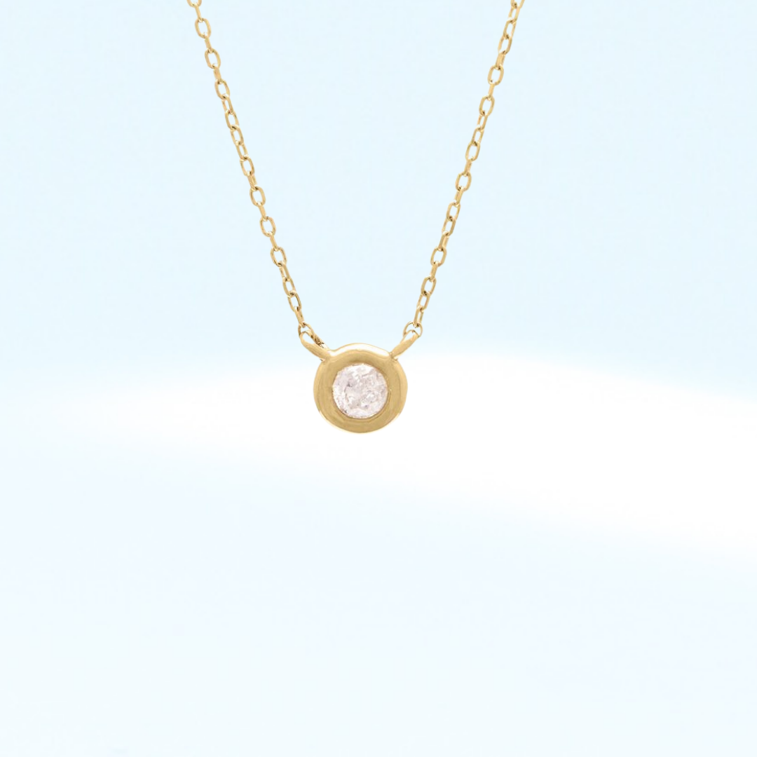 Gold necklace with a small round diamond bezel pendant on a light blue background