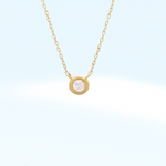 Gold necklace with a small round diamond bezel pendant on a light blue background
