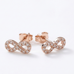 14K solid rose gold infinity stud earrings with natural diamond accents and push backs on white background.