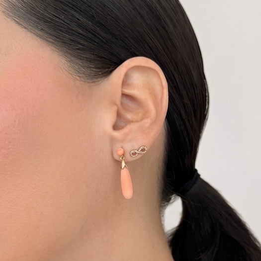 Close-up of ear styling featuring 14K solid rose gold infinity diamond stud earrings layered with soft pink coral drop earrings, styled with delicate gold necklaces for an elegant everyday luxury jewelry look.