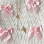 Necklace with religious charm surrounded by pink bows on a textured beige background