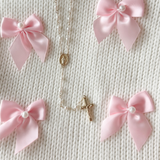 Necklace with religious charm surrounded by pink bows on a textured beige background