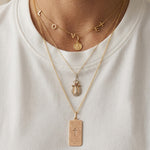 Close-up layered jewelry styling featuring a custom sideways cross letter necklace in 14K gold, paired with meaningful religious pendants and delicate layering chains for an elegant everyday luxury look.