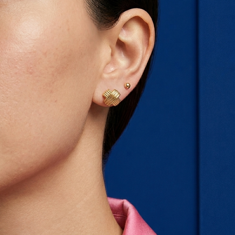 Close-up ear styling featuring 14K solid yellow gold vintage X stud earrings in a textured crisscross design paired with a minimalist gold ball stud for an elegant everyday luxury jewelry look.