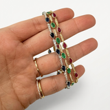 Hand wearing gold bracelets with colorful gemstones on a white background