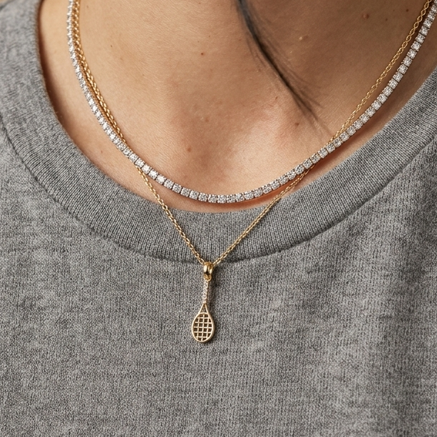 Model wearing a 14K solid yellow gold tennis racket pendant with sparkling clear CZ stones, layered with a tennis necklace, showcasing luxury tennis jewelry and athlete-inspired fine jewelry.
