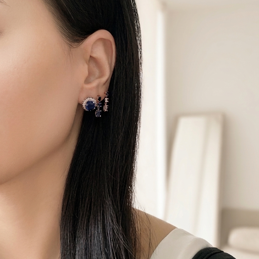 Woman wearing 18K yellow gold natural blue sapphire dangle earrings featuring oval and round sapphire gemstones.