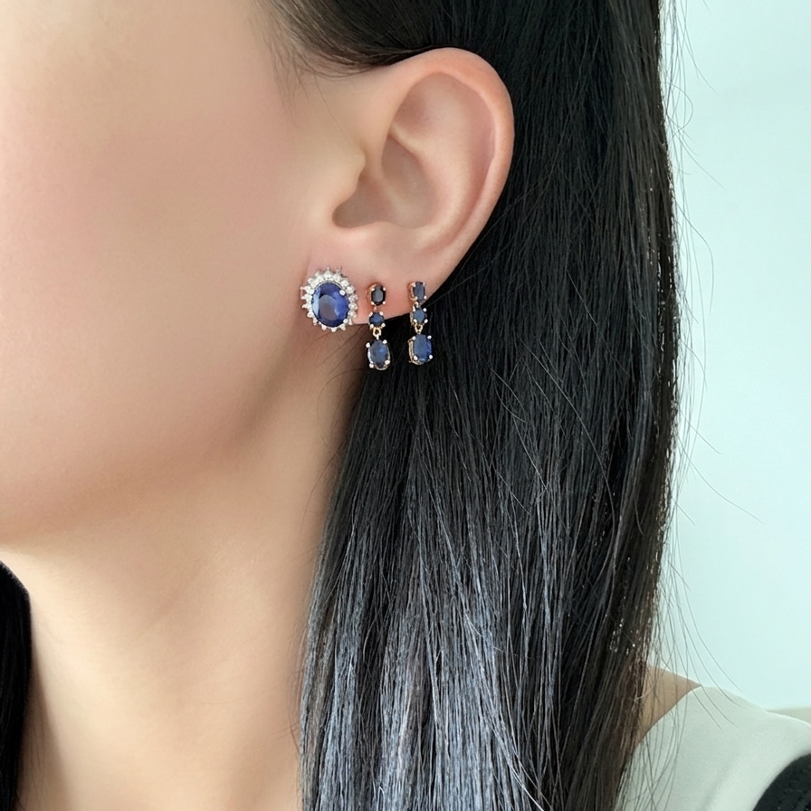 Woman wearing 18K yellow gold natural blue sapphire dangle earrings featuring oval and round sapphire gemstones.