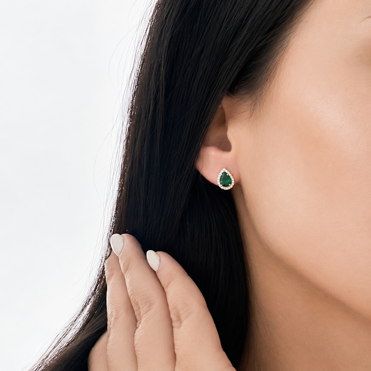 Woman wearing 14K solid yellow gold pear-shaped green emerald cubic zirconia halo stud earrings, featuring a vibrant emerald-green center stone surrounded by sparkling CZ accents.