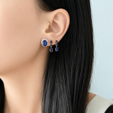 Woman wearing 18K yellow gold natural blue sapphire dangle earrings featuring oval and round sapphire gemstones.