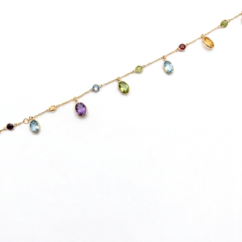 Woman wearing an 18K solid yellow gold multi-gemstone bracelet featuring natural garnet, blue topaz, citrine, peridot and amethyst dangling gemstone charms