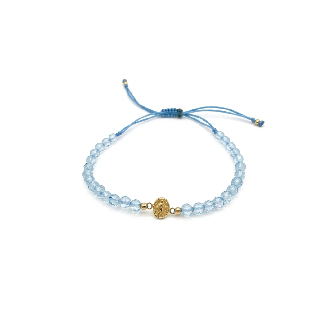 Blue macramé bracelet with faceted blue topaz gemstones and a gold miraculous medal charm, adjustable cord with gold bead accents.